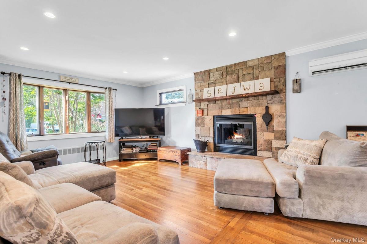 Hardwood flooring throughout, stone-clad fireplace with hearth and wood mantel, large multi-pane window, recessed lighting, and crown molding