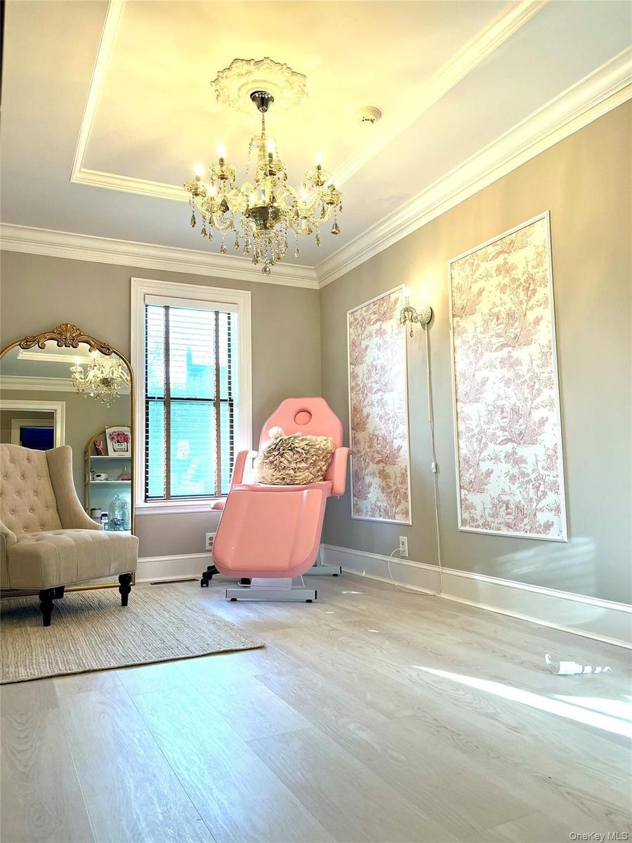 Elegant spa-inspired room featuring soaring coffered ceilings with recessed lighting, a crystal chandelier, light wood-finish flooring, and soft neutr