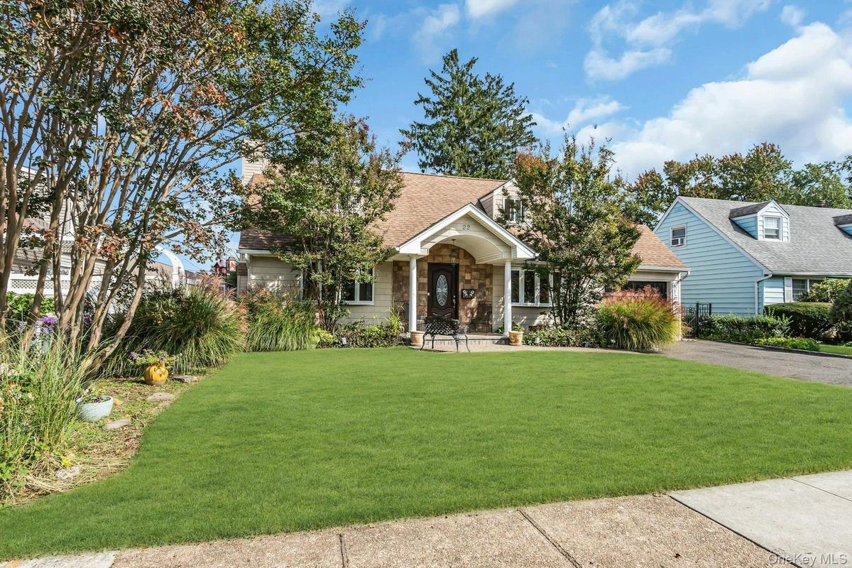 Manicured front lawn, stone facade, covered entry, and attached garage