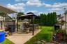 Expansive backyard featuring a concrete patio, freestanding gazebo, manicured lawn, and mature privacy trees