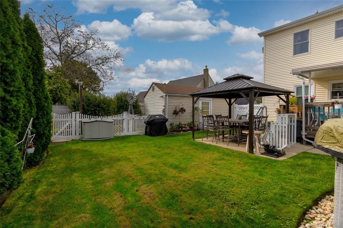 Expansive green lawn with a privacy hedge, white picket fencing, and a paved patio area