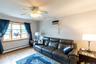 Light wood-finish flooring, ceiling fan with integrated lighting, window-mounted air conditioning unit, and bay window with wood trim