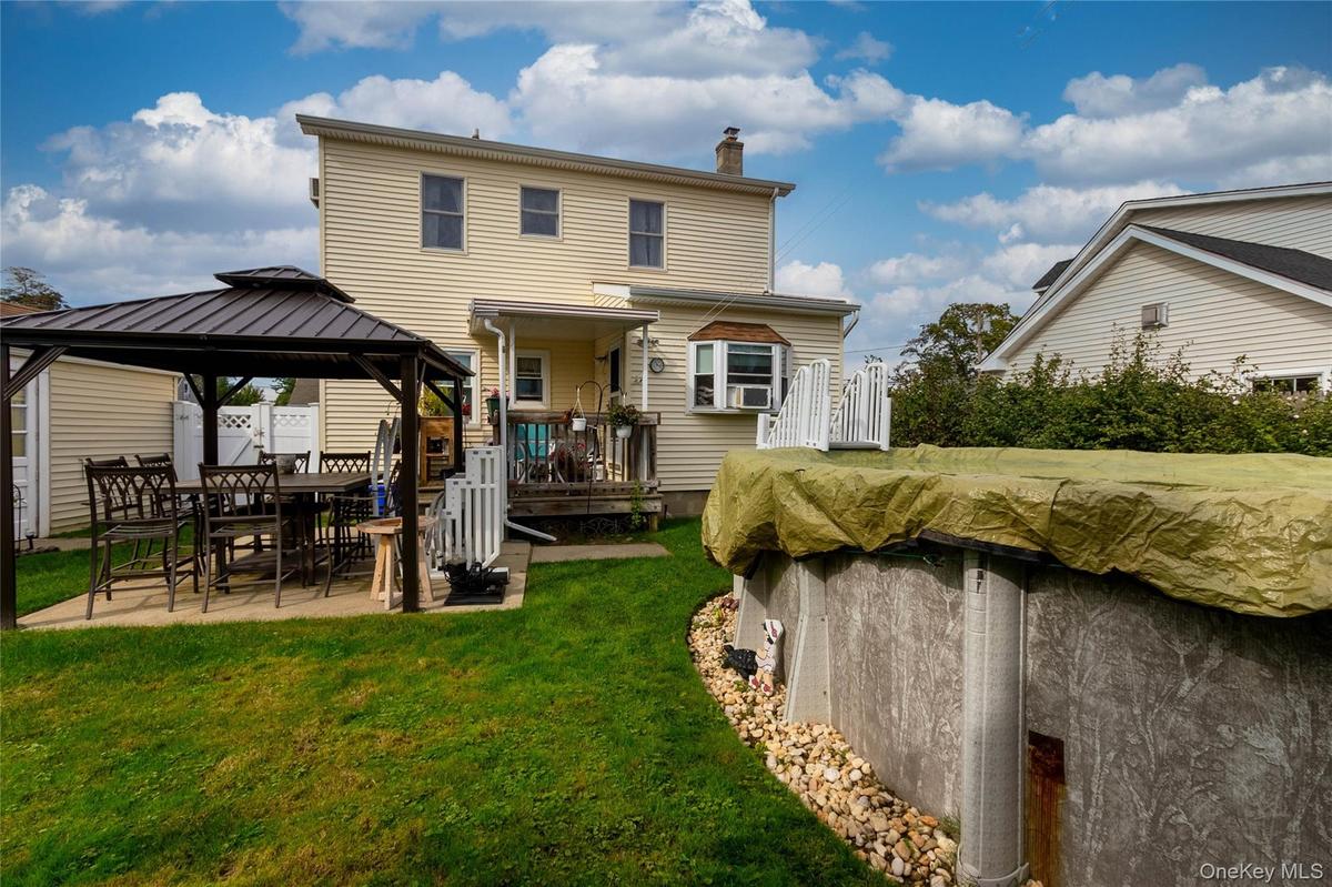 Expansive backyard featuring a covered patio, an above-ground pool, and a two-story residence with a bay window