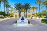 Paver driveway entrance featuring a prominent property sign with a tiered fountain, surrounded by mature palm trees and manicured landscaping