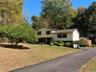 Siding exterior with dormer windows, surrounded by mature trees and landscaping, featuring a paved driveway and an expansive front lawn