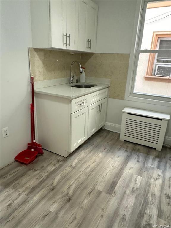 White shaker cabinetry, light-toned backsplash, stainless steel sink with a gooseneck faucet, light-toned countertop, and wood-finish flooring