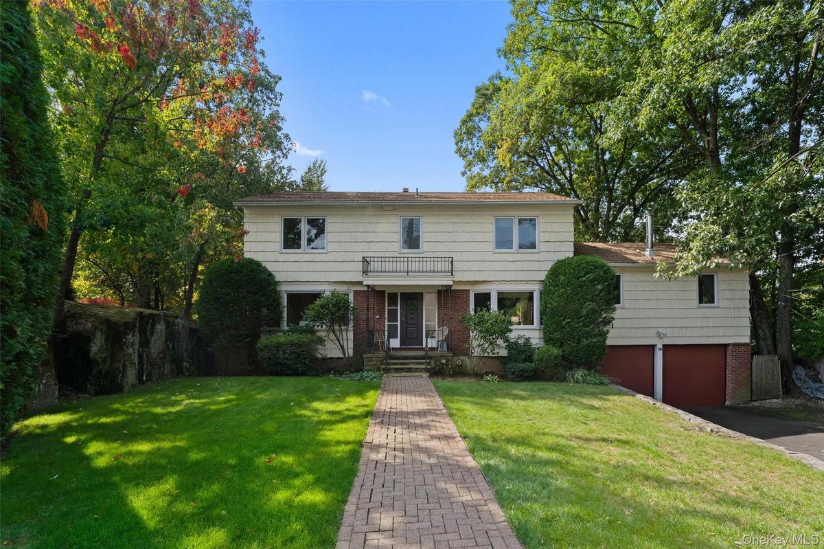 Welcome to 16 Cadillac Drive. Two-story residence with a brick paver walkway, mature trees, and a front lawn.