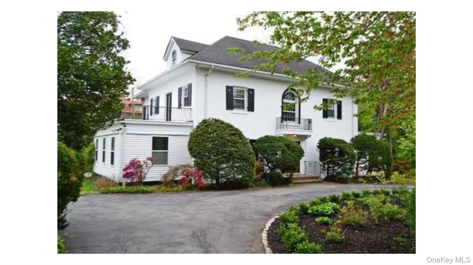 White exterior with black shutters, dormer window, second-story balcony with metal railing, and a paved driveway