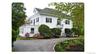 White exterior with black shutters, dormer window, second-story balcony with metal railing, and a paved driveway