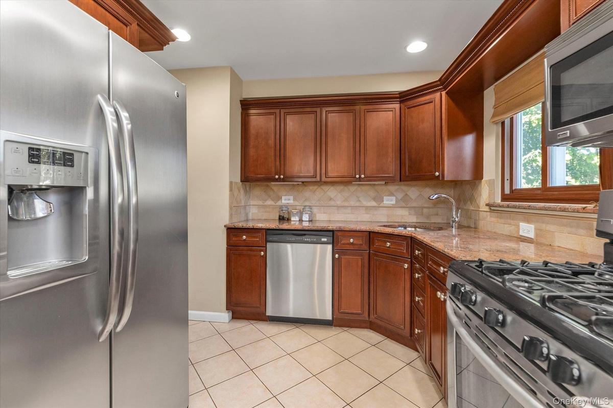 Kitchen featuring wood cabinetry, stainless steel appliances, tile flooring, and granite countertops