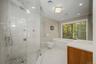 Light-filled primary bath with glass-enclosed steam shower, Bain Ultra tub, and serene woodland views.