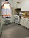 White cabinetry, gas range, metal range hood, stone-finish countertops, and tile flooring