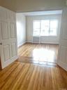 Hardwood flooring extending through an open doorway, white interior doors, and a window with a radiator below