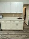 White upper and lower cabinetry, light-toned countertop, tile backsplash, and wood-finish flooring