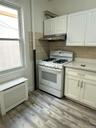 White shaker-style cabinetry, stainless steel range hood, tile backsplash, wood-finish flooring, and a white gas range