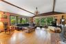 Vaulted ceiling with exposed wood beams, hardwood flooring, expansive window wall, brick fireplace, and a chandelier light fixture.