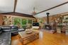 Vaulted ceiling with exposed wood beams, hardwood flooring, expansive window wall, brick fireplace, and a chandelier light fixture.