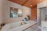 Tiled bathroom featuring a jacuzzi, built-in shower, vanity with  sink, and wall-mounted lighting.