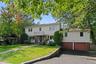 Welcome to 16 Cadillac Drive. Two-story residence with a brick paver walkway, mature trees, and a front lawn.