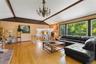 Vaulted ceiling with exposed wood beams, hardwood flooring, expansive window wall, brick fireplace, and a chandelier light fixture.