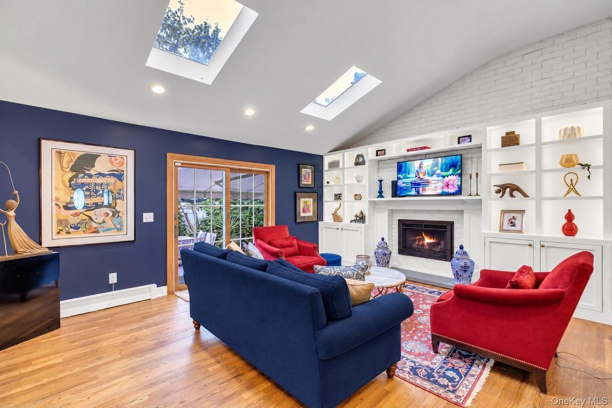 Vaulted ceiling with skylights, wood-finish flooring, built-in shelving, and a gas fireplace