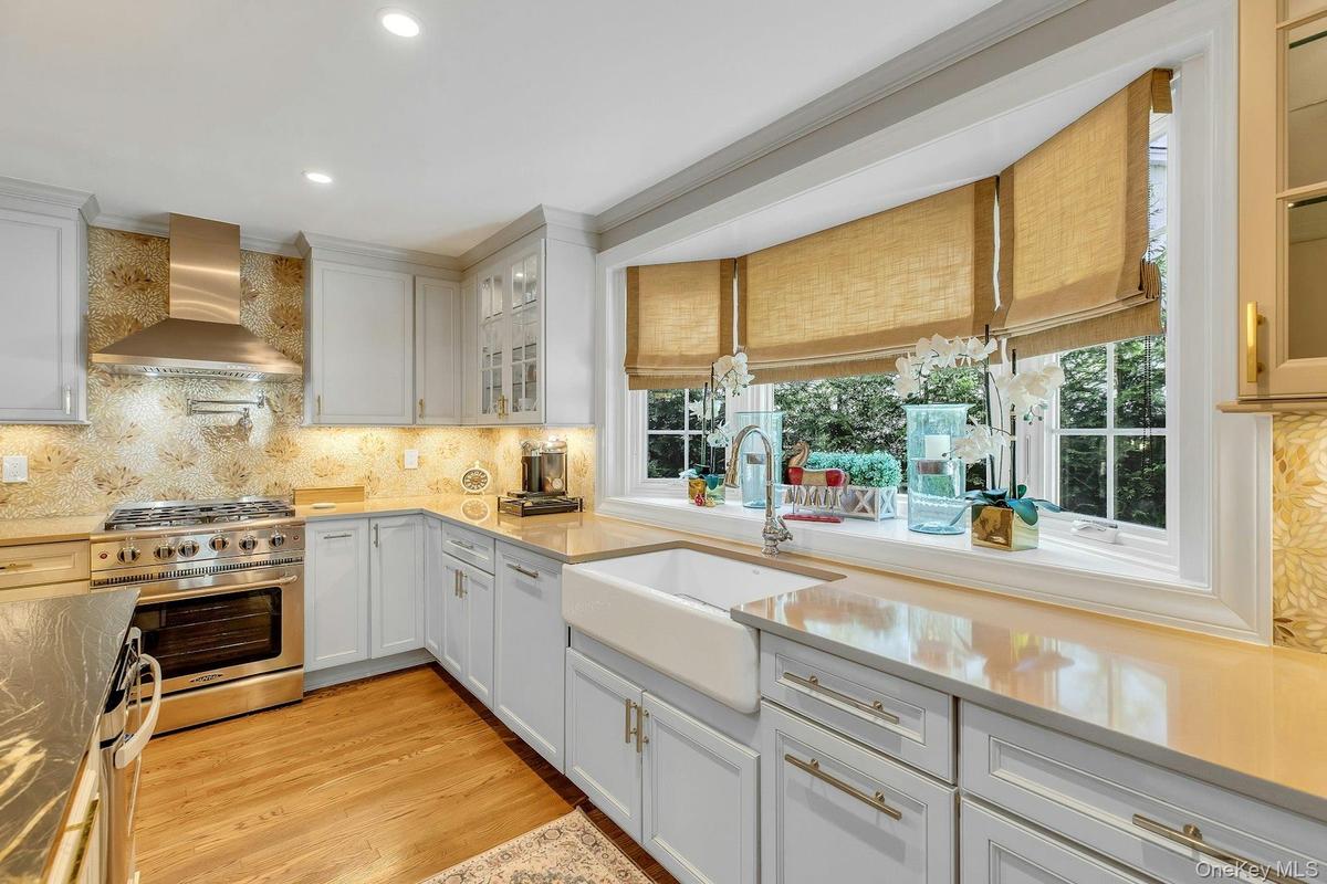 White cabinetry, light countertops, wood-finish flooring, stainless steel range with hood, and a farmhouse sink