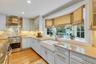 White cabinetry, light countertops, wood-finish flooring, stainless steel range with hood, and a farmhouse sink
