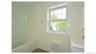 White bathtub with a curved glass shower partition, white window with grid panes, textured wall covering, and a white vanity with an integrated sink