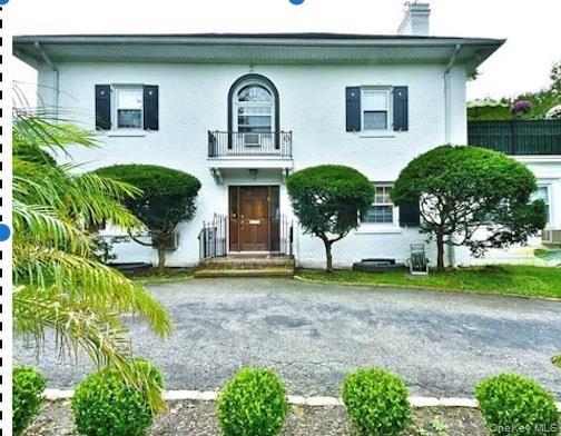 White stucco exterior with black functional shutters, front entry with transom window, second-story Juliet balcony, and paved driveway