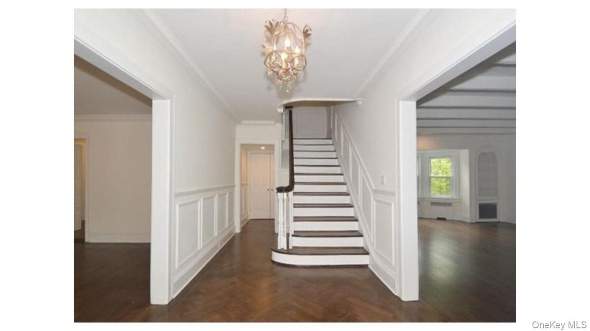Wood-finish flooring, staircase with dark wood handrail, decorative chandelier, wainscoting paneling, and coffered ceilings