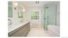 Dual vanity with integrated sinks, frameless glass shower enclosure, freestanding soaking tub, and natural light from a double-hung window