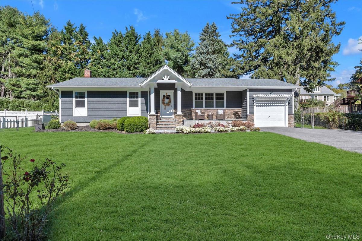 Shingle siding exterior with stone accents, a covered front porch, an attached garage, a paved driveway, and a front lawn