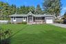 Shingle siding exterior with stone accents, a covered front porch, an attached garage, a paved driveway, and a front lawn