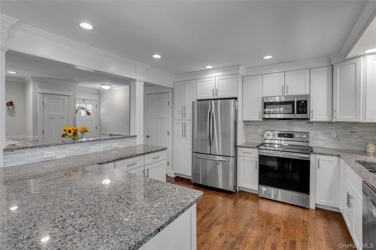 Granite countertops, white shaker cabinetry, stainless steel appliances, wood-finish flooring, and recessed lighting