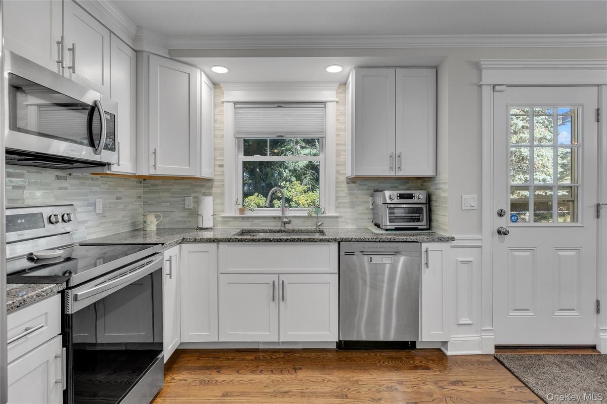 Kitchen featuring white cabinetry, stainless steel appliances, granite countertops, a tiled backsplash, and wood-finish flooring, access to backyard r