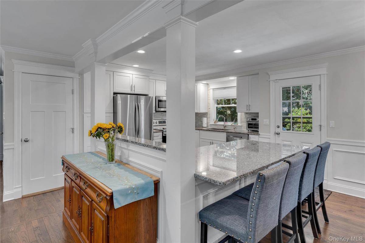 Bright, open-concept kitchen and dining area featuring white cabinetry, stainless steel appliances, quartz countertops, and a large center island with