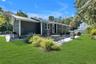 Expansive backyard featuring a manicured lawn, paver patio, mature trees, and dark gray siding