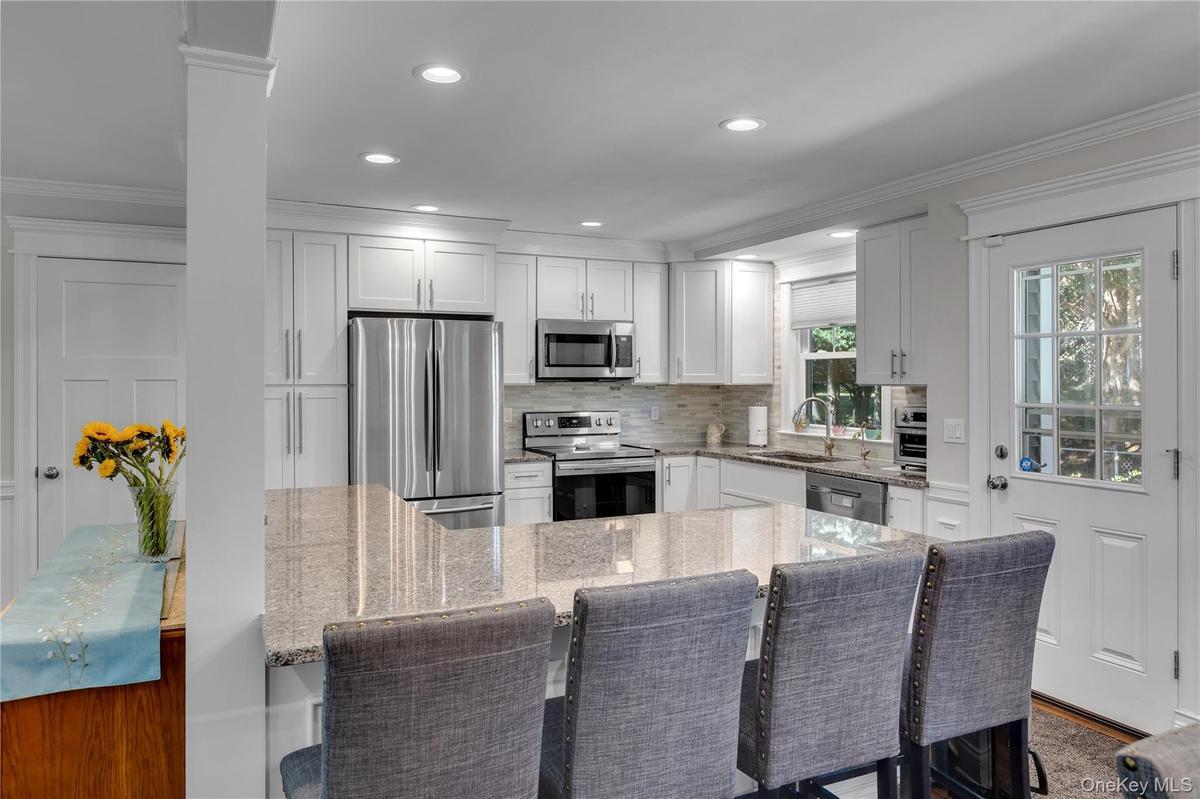 Kitchen featuring white cabinetry, stainless steel appliances, a large island with a stone countertop, and a glass-paned exterior door