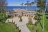 Brick exterior with a multi-car garage, expansive manicured lawn, gravel circular driveway, and mature landscaping