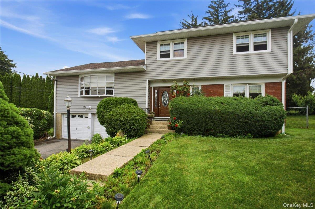 Split-level residence featuring gray siding, red brick accents, an arched front door, and a two-car garage