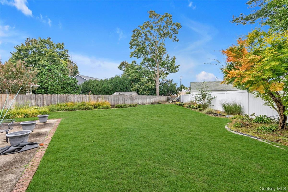 Expansive lawn area with a mix of wood and vinyl fencing, mature trees, and a concrete patio with brick edging