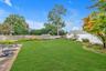 Expansive lawn area with a mix of wood and vinyl fencing, mature trees, and a concrete patio with brick edging