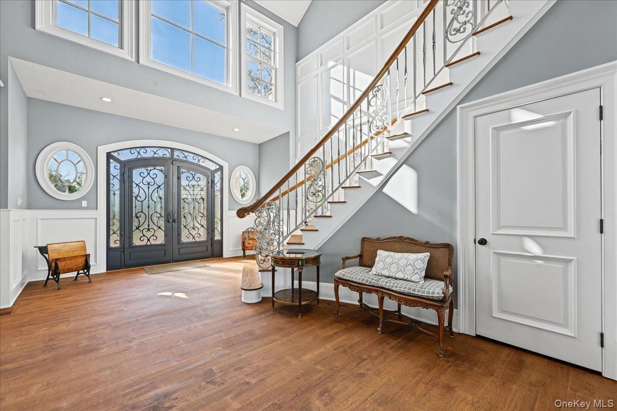 Grand entryway featuring a decorative double-door entry, a substantial staircase with wrought iron balusters, hardwood flooring, and wainscoting