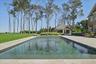 Expansive outdoor area featuring a swimming pool, a large patio, a separate pool house structure, a vast lawn, and mature trees