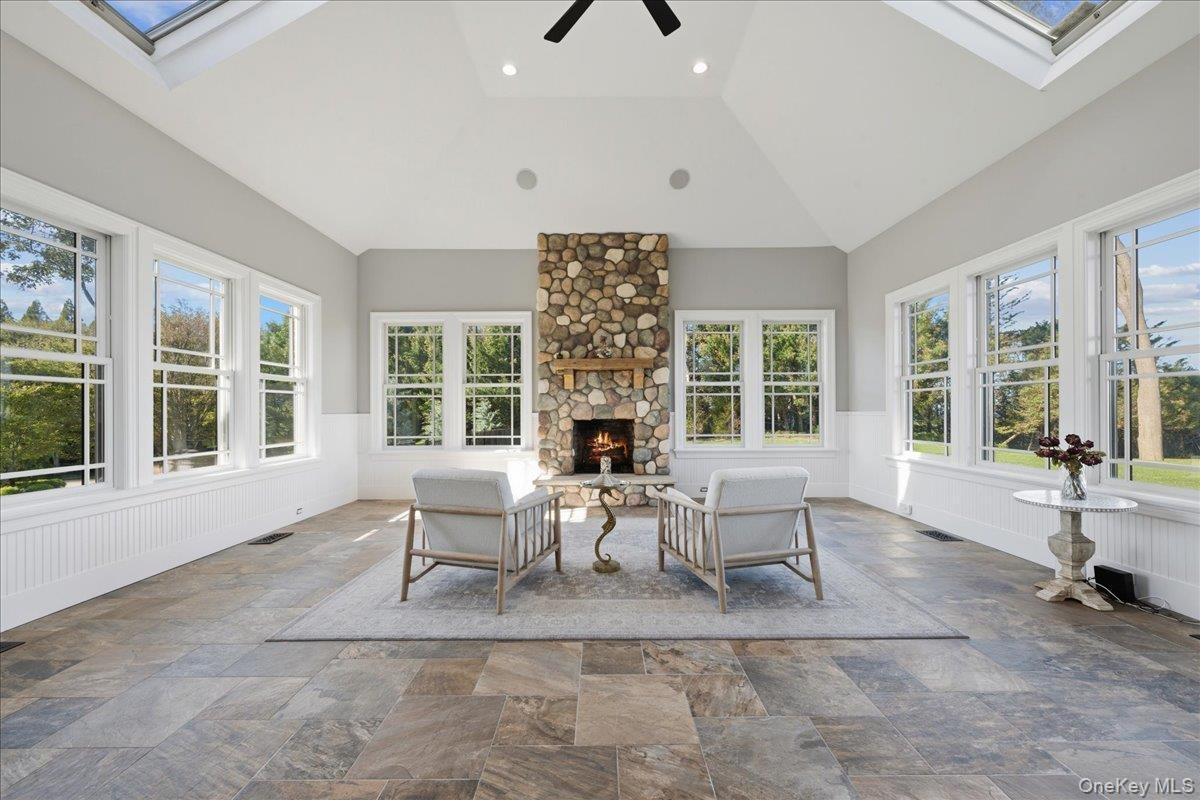 Vaulted ceiling with skylights, stone fireplace with wood mantel, tile flooring, and multiple windows with white trim