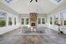 Vaulted ceiling with skylights, stone fireplace with wood mantel, tile flooring, and multiple windows with white trim