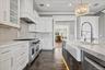 White cabinetry with glass-front uppers, stainless steel range, light-toned subway tile backsplash, and a farmhouse sink with a gooseneck faucet