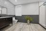 Modern bathroom featuring wood-finish flooring, a freestanding vanity with gold-tone hardware, a frameless shower enclosure, and a window with blinds
