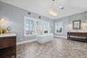 Hexagonal tile flooring, freestanding soaking tub, dual wood-finish vanity with countertop, textural accent wall, and multiple windows