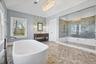 Freestanding soaking tub, walk-in shower with glass enclosure, wood-finish vanity with dual sinks, mosaic tile accent wall, and hexagonal floor tiling